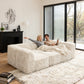 Soft sand daybed –showcased in a modern cozy living room setting. A model sits on it to demonstrate scale and comfort