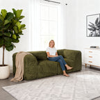 Olive green Modular Loveseat–showcased in a modern cozy living room setting. A model sits on it to demonstrate scale and comfort
