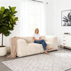 Soft sand Modular Loveseat–showcased in a modern cozy living room setting. A model sits on it to demonstrate scale and comfort