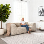 Taupe gray loveseat –showcased in a modern cozy living room setting. A model sits on it to demonstrate scale and comfort