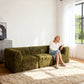 Olive green sofa –showcased in a modern cozy living room setting. A model sits on it to demonstrate scale and comfort